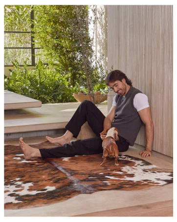 Man sitting with his dog on a cowhide rug, enjoying a cozy moment together in the living room