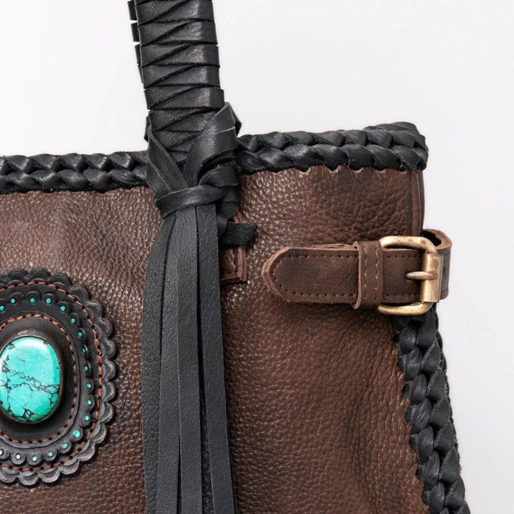 Close-up of the Black Braided Leather Tote showing intricate braiding, a turquoise stone embellishment, and an antique brass buckle.