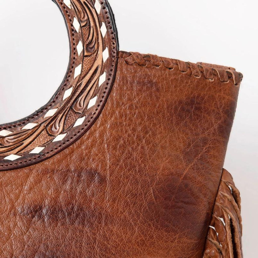 Close-up of the Canyon Breeze Leather Tote's hand-tooled circular handle and leather stitching details.