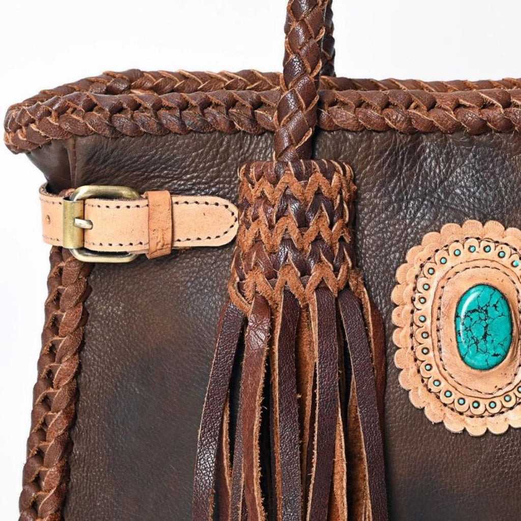 Close-up of the Braided Sage Western Leather Tote in Chestnut Brown, highlighting the intricate braided leather design, turquoise stone centerpiece, and adjustable buckle detail.