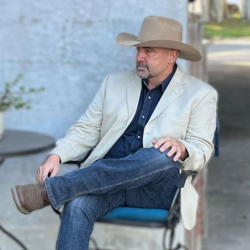 Man wearing the Dakota Range Chestnut Cowboy Hat, made from a luxurious blend of fine Bolivian cashmere and wool, featuring a Cattleman crown and traditional brim. Styled with a light blazer, denim shirt, and jeans in an outdoor setting.