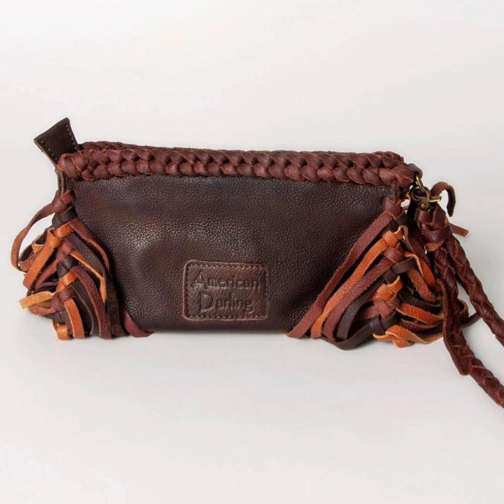 The back of a dark brown western-style leather clutch with braided details, fringes, and a stitched "American Darling" brand patch.