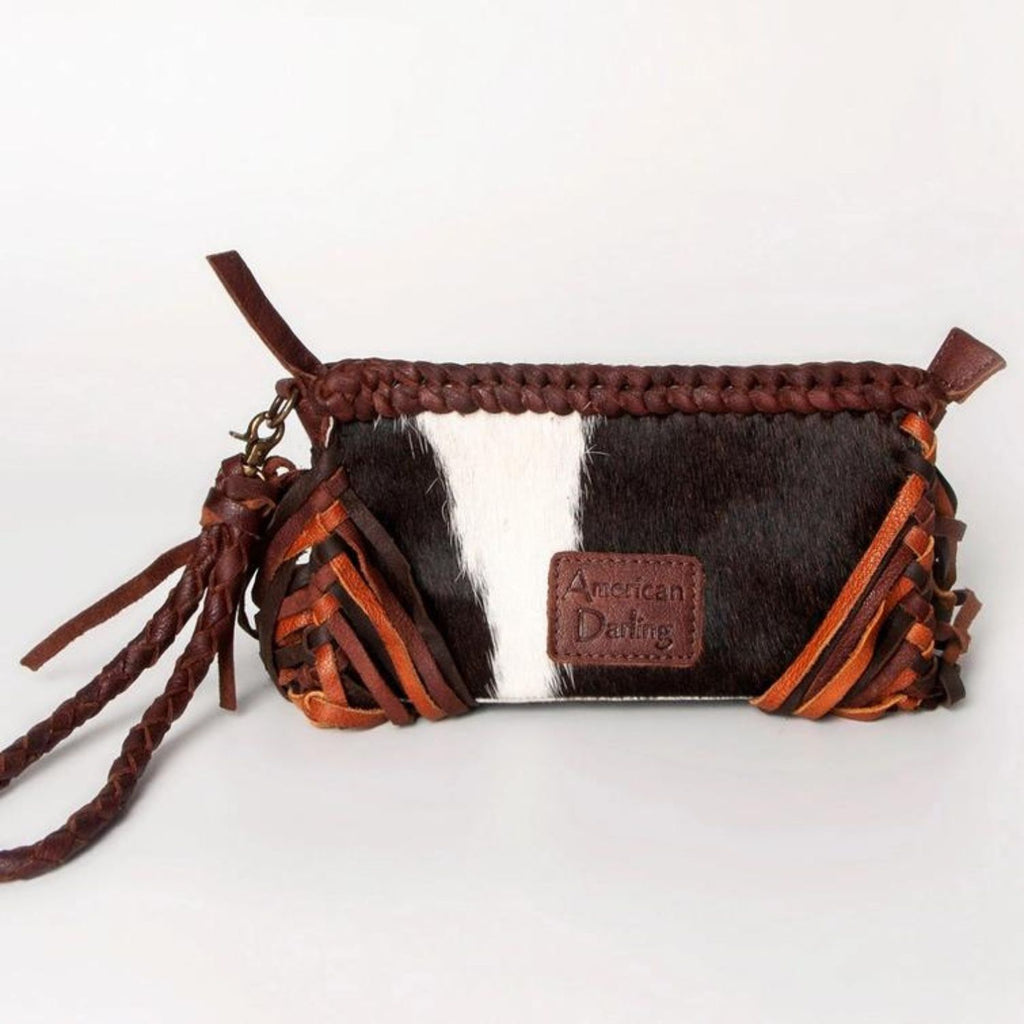 The back of a handcrafted western-style leather clutch featuring hair-on leather with brown and white tones, braided details, and the American Darling brand patch.