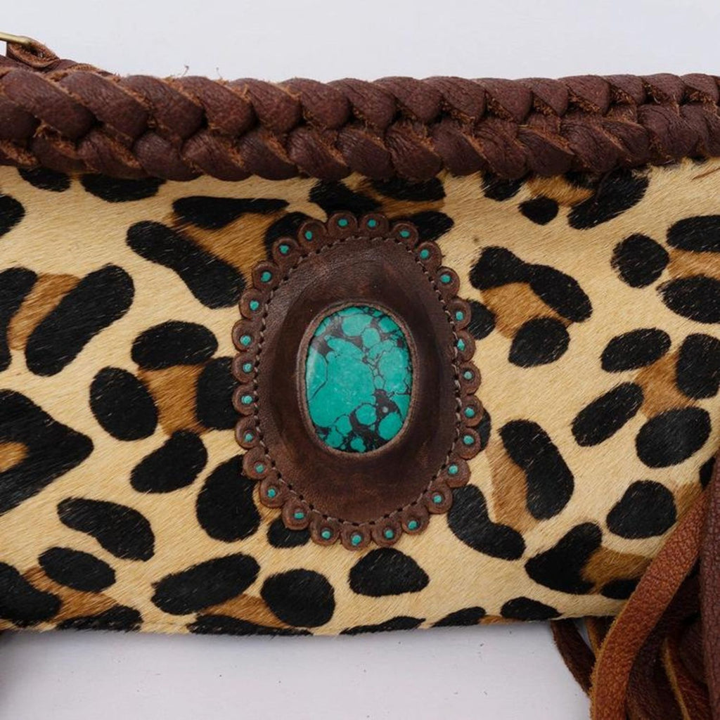 Close-up of a leopard print hair-on leather clutch featuring braided details and a turquoise stone centerpiece.