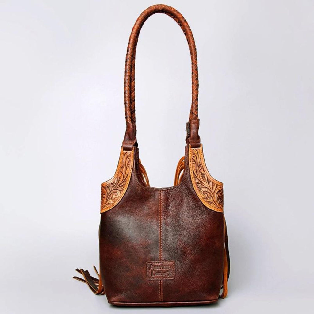 Back view of a hand-tooled leather Western tote bag featuring braided shoulder straps and detailed carving.