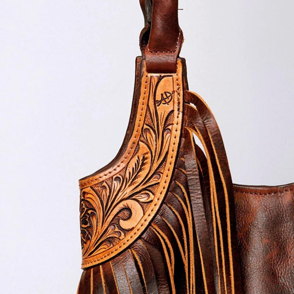 Close-up of the hand-tooled leather detailing on the strap of a Western tote bag, showcasing intricate craftsmanship and fringe accents.