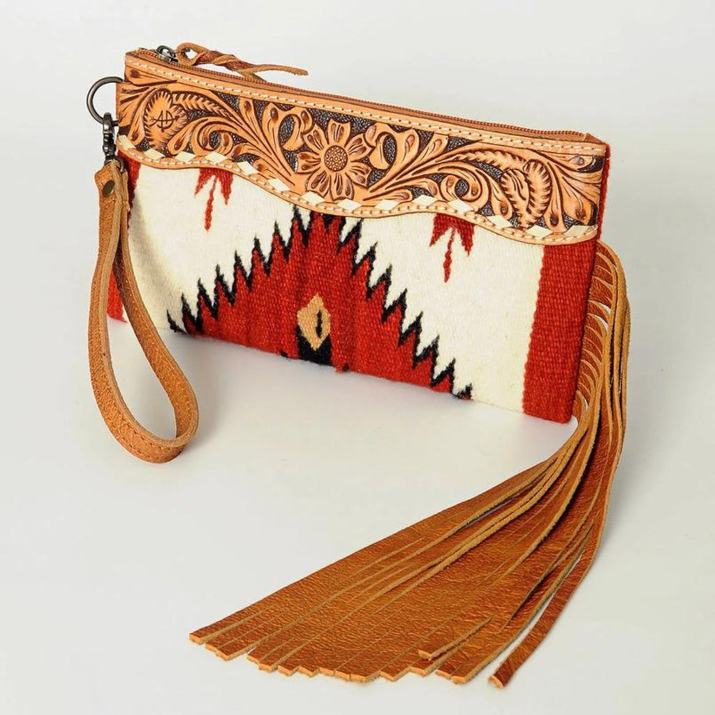 Prairie Rose Leather Wristlet with intricate floral tooled leather trim and vibrant southwestern woven fabric in red, white, and tan, featuring a long leather fringe and detachable wrist strap.