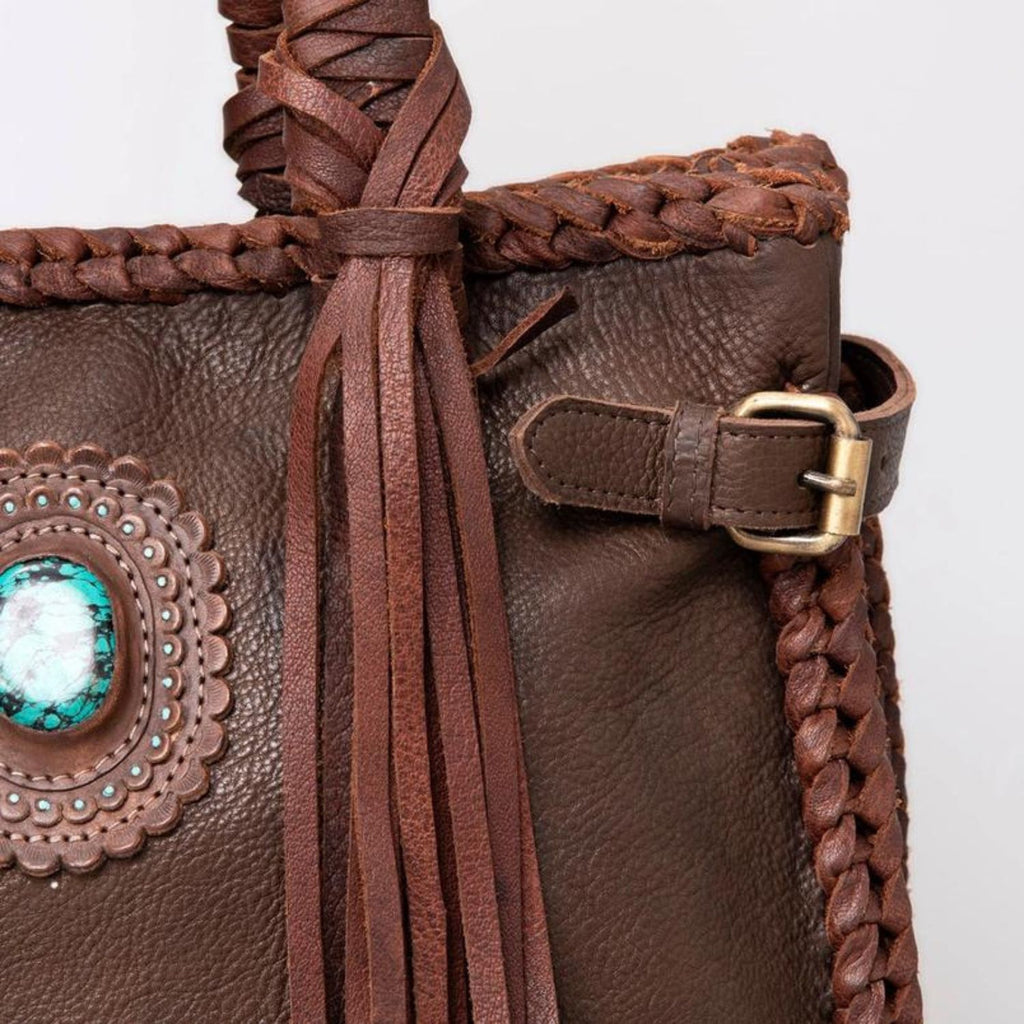 Close-up of the Saddle Brown Western Braided Leather Tote showcasing intricate braiding, fringes, and turquoise stone detail.