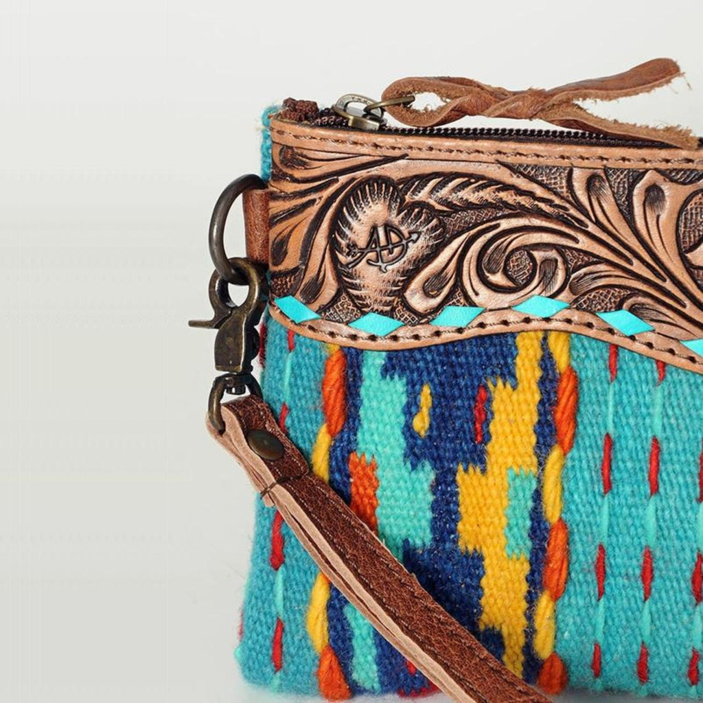 Close-up view of the Sierra Sky Leather Fringe Bag featuring intricate leather tooling with a floral design, accented by a turquoise lace trim and colorful woven fabric.