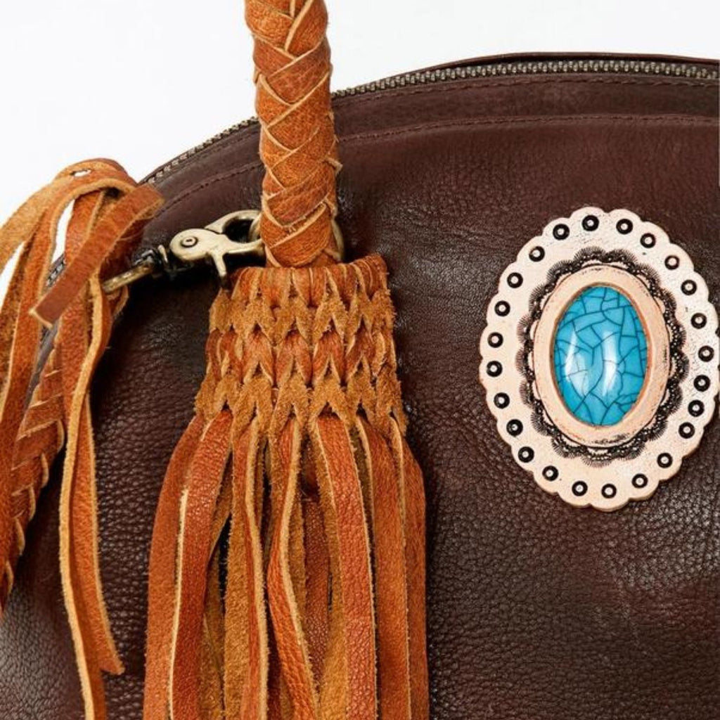 Close-up detail view of the Turquoise Trail Fringed Leather Tote, highlighting the braided handle, leather fringe, and turquoise stone embellishment in a Western-inspired design.