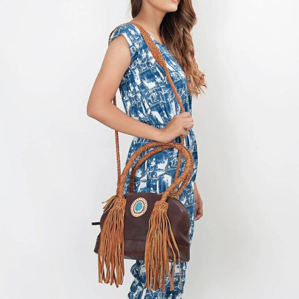 Model wearing the Turquoise Trail Fringed Leather Tote with braided handles, leather fringe, and turquoise stone detailing, showcasing its Western style and adjustable shoulder strap.