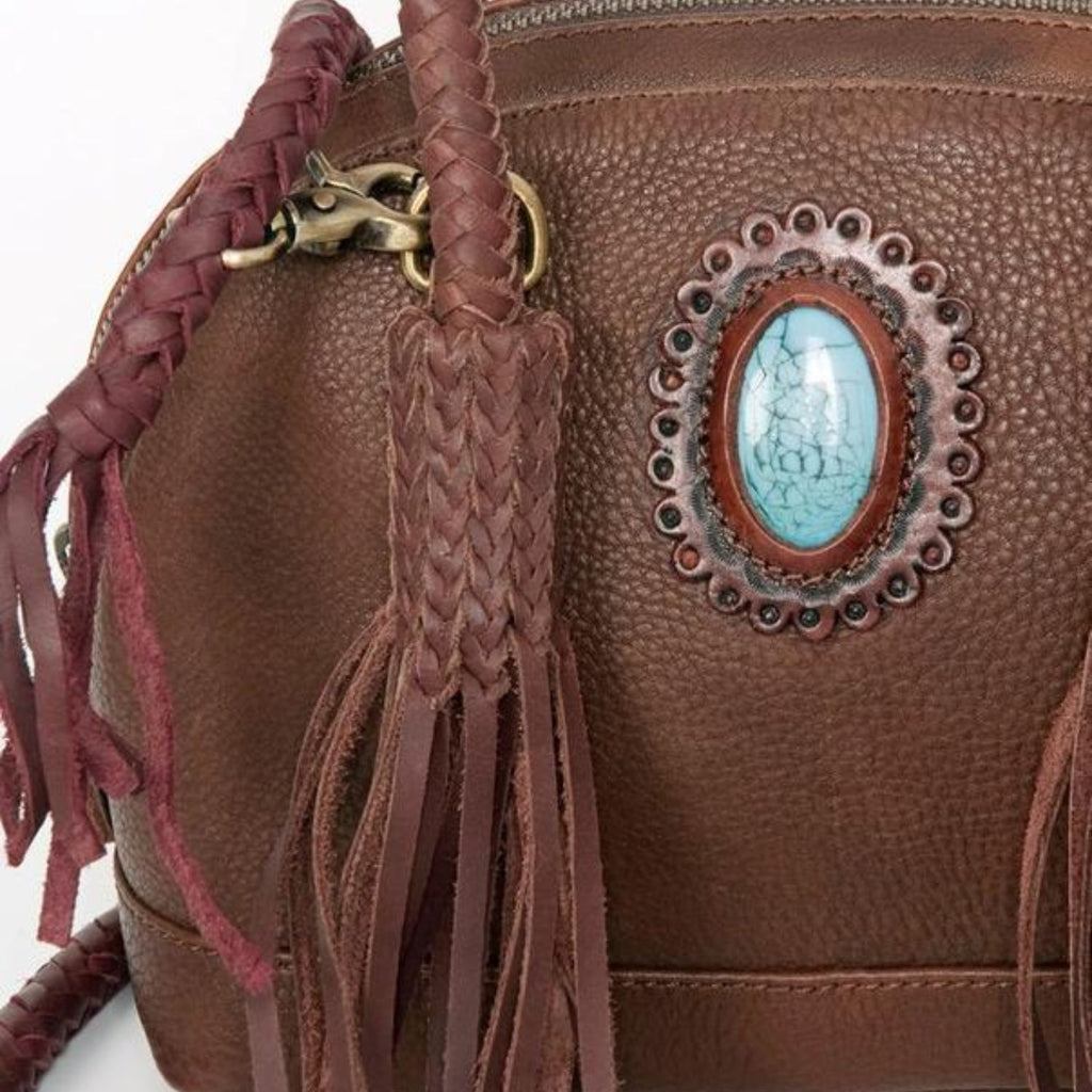 Close-up detail view of a variant of the Turquoise Trail Fringed Leather Tote, showcasing the braided handle, leather fringe, and turquoise stone embellishment in a rich leather finish.